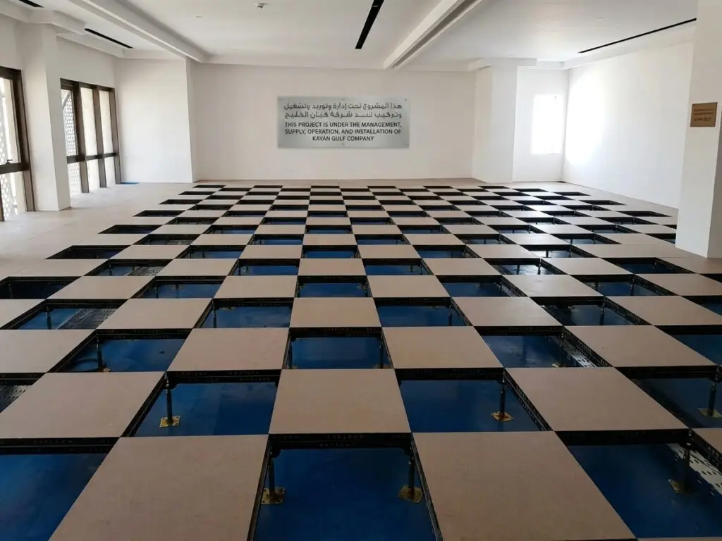 Raised access flooring system with underfloor structures and pedestal stands installed by Kayan Gulf Company in a commercial building.